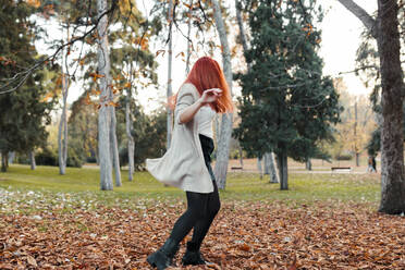 Carefree woman with brown hair dancing on land in park during autumn - MRRF00777