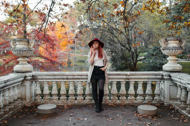 Thoughtful beautiful woman wearing hat while leaning on railing against lake - MRRF00782