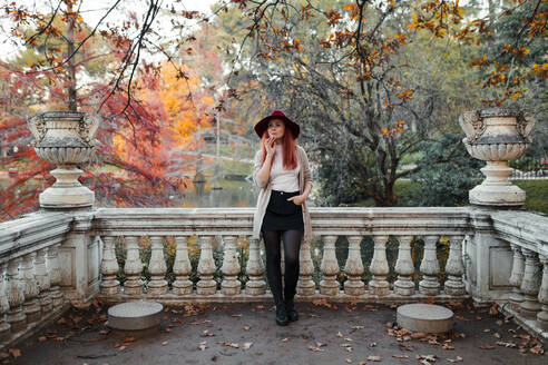 Thoughtful beautiful woman wearing hat while leaning on railing against lake - MRRF00782