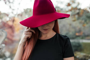 Nahaufnahme einer mittleren erwachsenen Frau mit rotem Hut im Park - MRRF00784