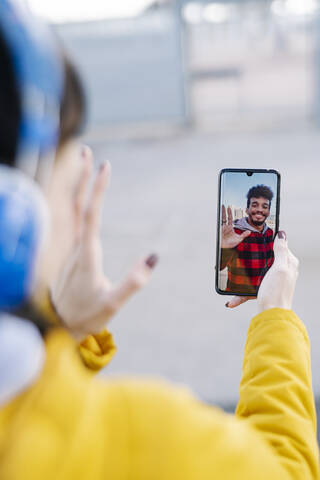 Young woman waving hand to friend on video call while standing outdoors stock photo