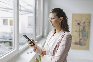 Businesswoman using smart phone in office - GUSF04951