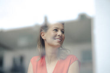 Smiling businesswoman looking through window - GUSF04964