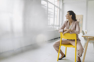 Lächelnde Geschäftsfrau sitzt auf einem Stuhl in einem leeren Büro - GUSF04980