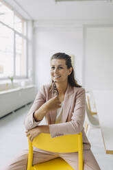 Portrait of smiling businesswoman sitting on chair in empty office - GUSF04983