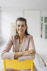 Portrait of smiling businesswoman sitting on chair in empty office - GUSF04984