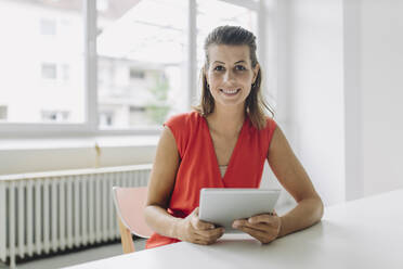 Portrait of businesswoman with digital tablet sitting in office - GUSF05017