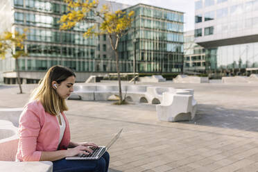 Spain, Barcelona, Young businesswoman using laptop in front of office buildings - XLGF00948