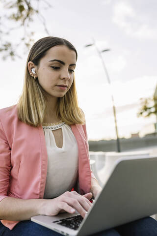 Young businesswoman using laptop outdoors stock photo