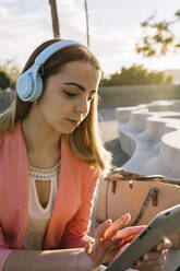 Junge Frau mit Kopfhörern, die im Freien ein digitales Tablet benutzt - XLGF00960