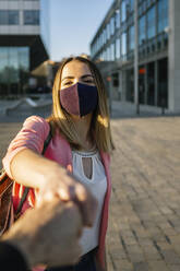 Woman wearing face mask greeting person with a fist bump in the city - XLGF00963