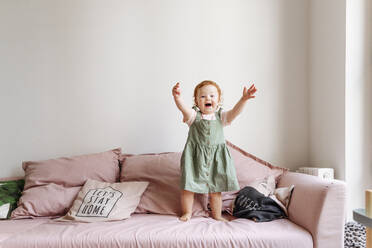 Lächelndes kleines Mädchen, das mit erhobenen Armen auf dem Sofa steht - VYF00377