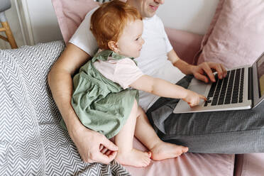 Mann mit kleiner Tochter arbeitet am Laptop auf dem Sofa - VYF00397