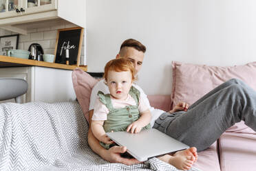 Mann mit kleiner Tochter auf Sofa mit Laptop - VYF00399