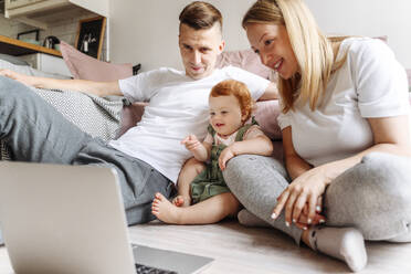 Happy family with baby daughter looking at laptop at home - VYF00400