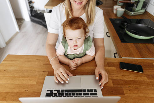 Frau mit kleiner Tochter benutzt Laptop am Küchentisch - VYF00402