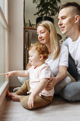 Happy family with baby daughter looking through window - VYF00405