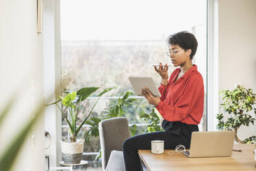 Frau benutzt Smartphone und digitales Tablet am Tisch mit Laptop zu Hause - UUF22473