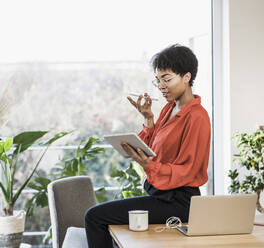 Frau benutzt Smartphone und digitales Tablet am Tisch mit Laptop zu Hause - UUF22474