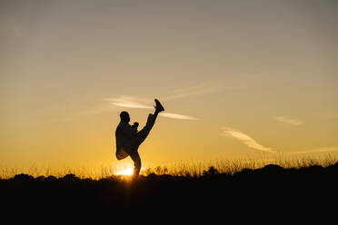 Silhouette of man practicing martial arts against setting sun - EGAF01438