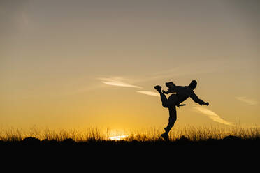 Silhouette of man practicing martial arts against setting sun - EGAF01440