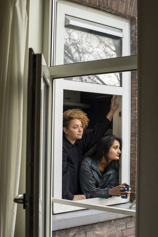 Lesbian couple looking together through window stock photo
