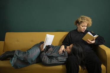 Lesbian couple reading books on sofa - AXHF00067