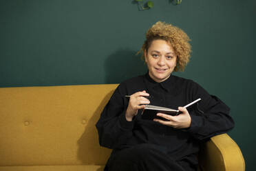 Portrait of young woman sitting on sofa with note pad in hands - AXHF00070