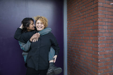 Young woman piggybacking girlfriend in front of building entrance stock photo