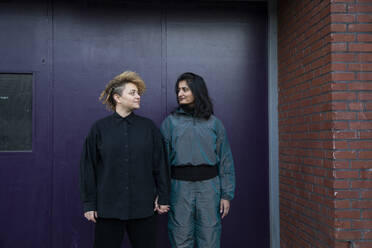 Lesbisches Paar hält sich vor einem Gebäudeeingang an den Händen - AXHF00094