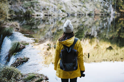 Woman in yellow raincoat facing river and waterfall stock photo