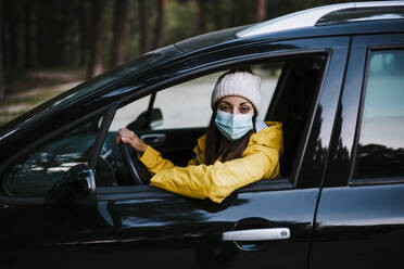 Frau mit gelbem Regenmantel und Gesichtsmaske sitzt im Auto - EBBF02117