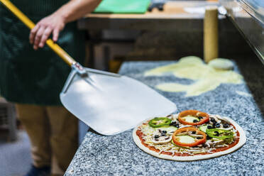 Tiefschnitt eines Kochs, der eine rohe Pizza mit einem Pizzaschieber aufnimmt - DLTSF01483