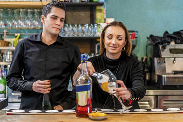 Female bartender preparing cocktail with male assistant - DLTSF01495