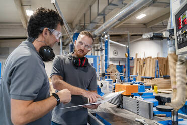 Zwei männliche Tischler sprechen über Dokumente in einer Produktionshalle - DIGF14170