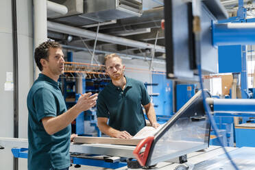 Two male carpenters working together next to circular saw in production hall - DIGF14182