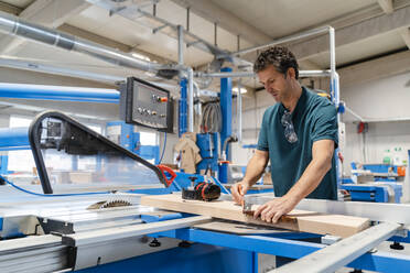 Carpenter measuring plank in front of circular saw - DIGF14183