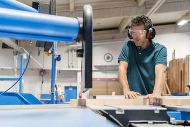 Carpenter cutting plank on circular saw in production hall - DIGF14185