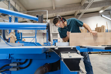 Carpenter cutting plank on circular saw in production hall - DIGF14186