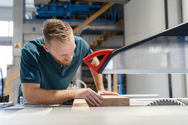 Carpenter cutting plank on circular saw in production hall - DIGF14187