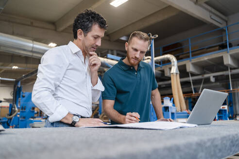 Zwei Zimmerleute sprechen über Dokumente in der Produktionshalle - DIGF14194