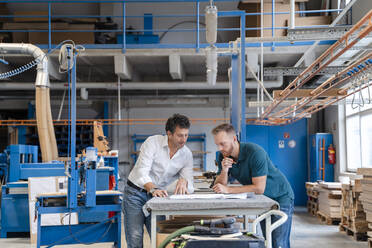 Two carpenters talking over documents in production hall - DIGF14195