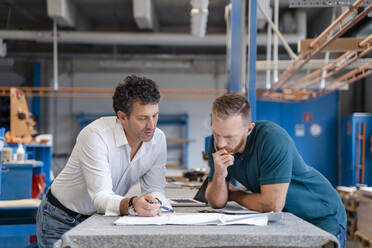 Two carpenters talking over documents in production hall - DIGF14196