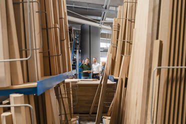 Two carpenters talking in production hall with wooden planks in foreground - DIGF14214