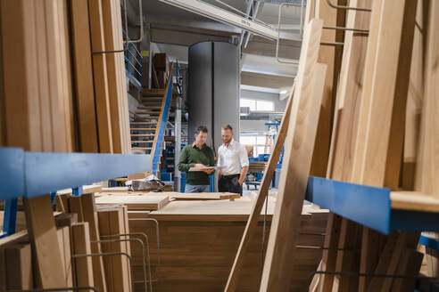 Zwei Zimmerleute unterhalten sich in einer Produktionshalle mit Holzbrettern im Vordergrund - DIGF14215