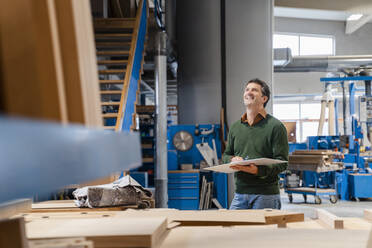 Carpenter standing in production hall with ring binder in hands - DIGF14217