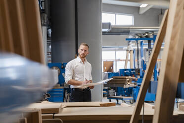 Carpenter standing in production hall with ring binder in hands - DIGF14218