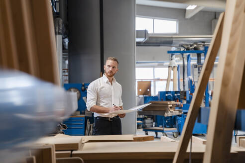 Schreiner in der Produktionshalle mit Ringbuch in der Hand - DIGF14218