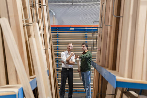 Zwei Zimmerleute unterhalten sich in einer Produktionshalle mit Holzbrettern im Vordergrund - DIGF14221