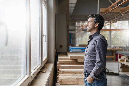 Porträt eines Zimmermanns, der durch ein Fenster in einer Produktionshalle schaut - DIGF14227